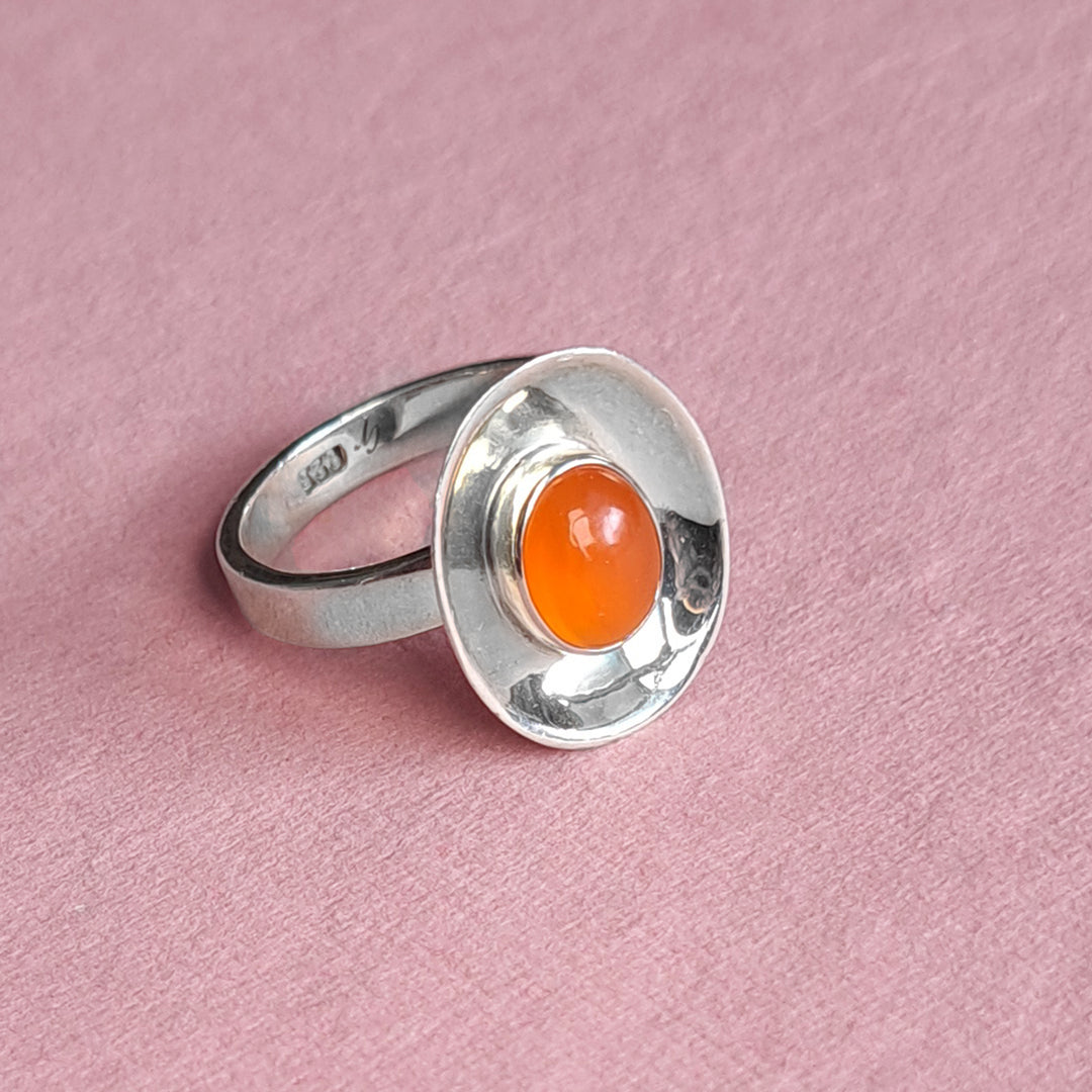 Sterling silver dish shaped ring set with a carnelian cabochon gemstone on a pink background