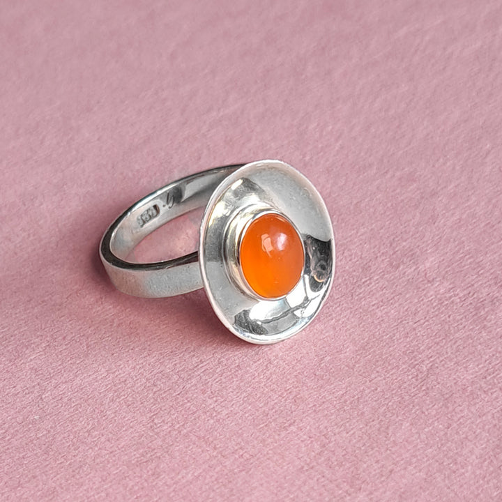 Sterling silver dish shaped ring set with a carnelian cabochon gemstone on a pink background