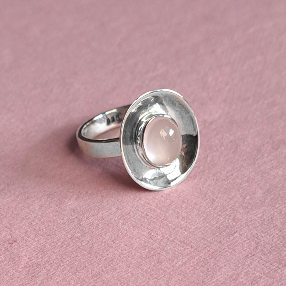 Sterling silver dish shaped ring with rose quartz cabochon gemstone on a pink background