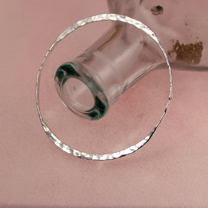 Sterling silver double take bangle with hammered texture with a bottle on a pink background