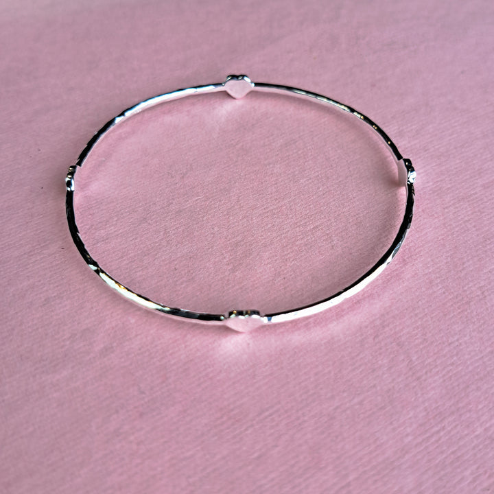 Sterling silver four heart hammered bangle on a pink paper background