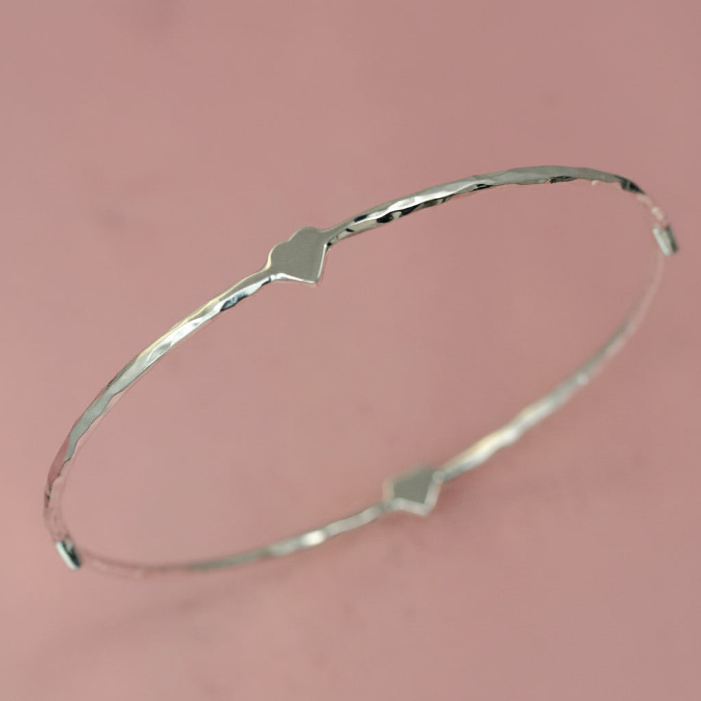 Sterling silver four heart hammered bracelet on a pink background