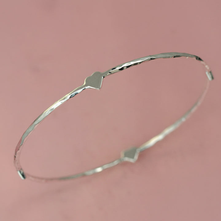 Sterling silver four heart hammered bracelet on a pink background
