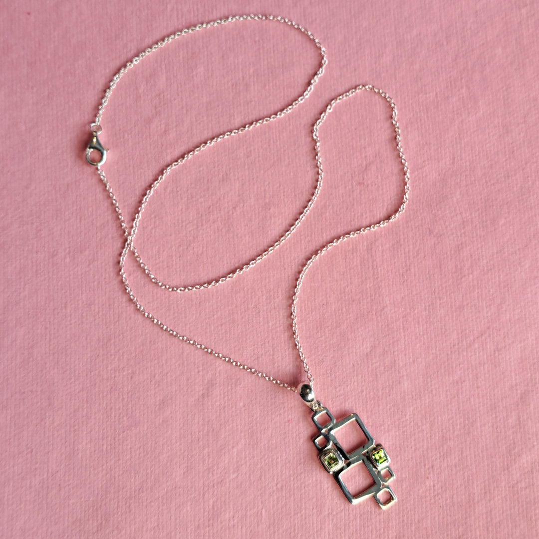 Sterling silver geometric pendant necklace with peridot cabochons on a pink background