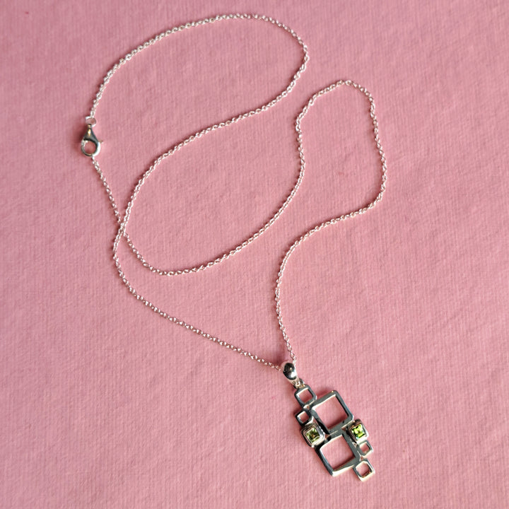 Sterling silver geometric pendant necklace with peridot cabochons on a pink background
