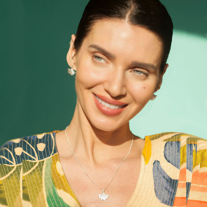 Woman wearing a colorful patterned top with a silver ginkgo necklace and matching earrings