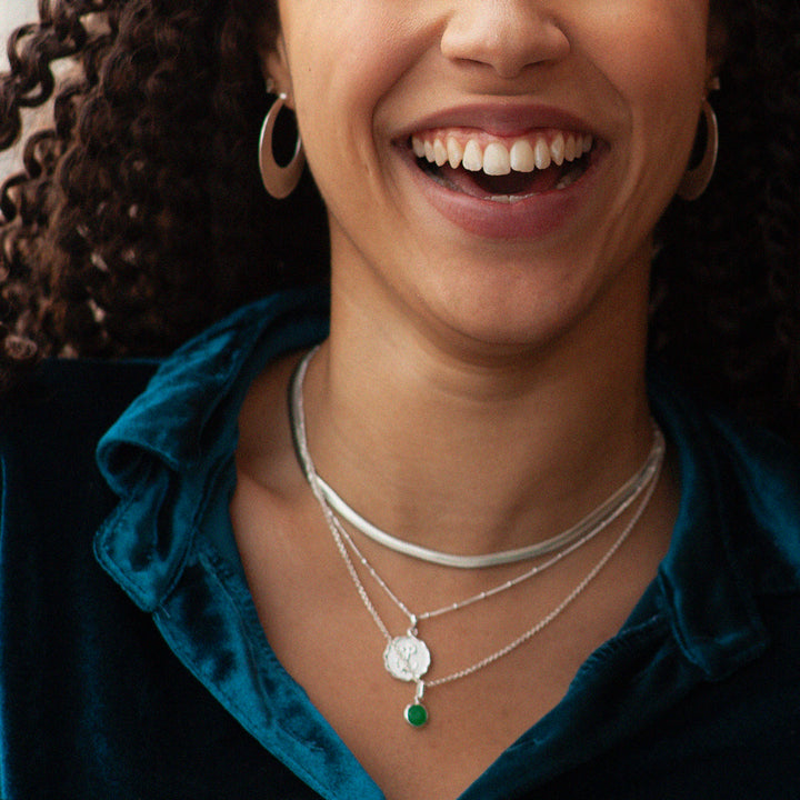 Model wearing several silver necklaces with a green quartz birthstone pendant