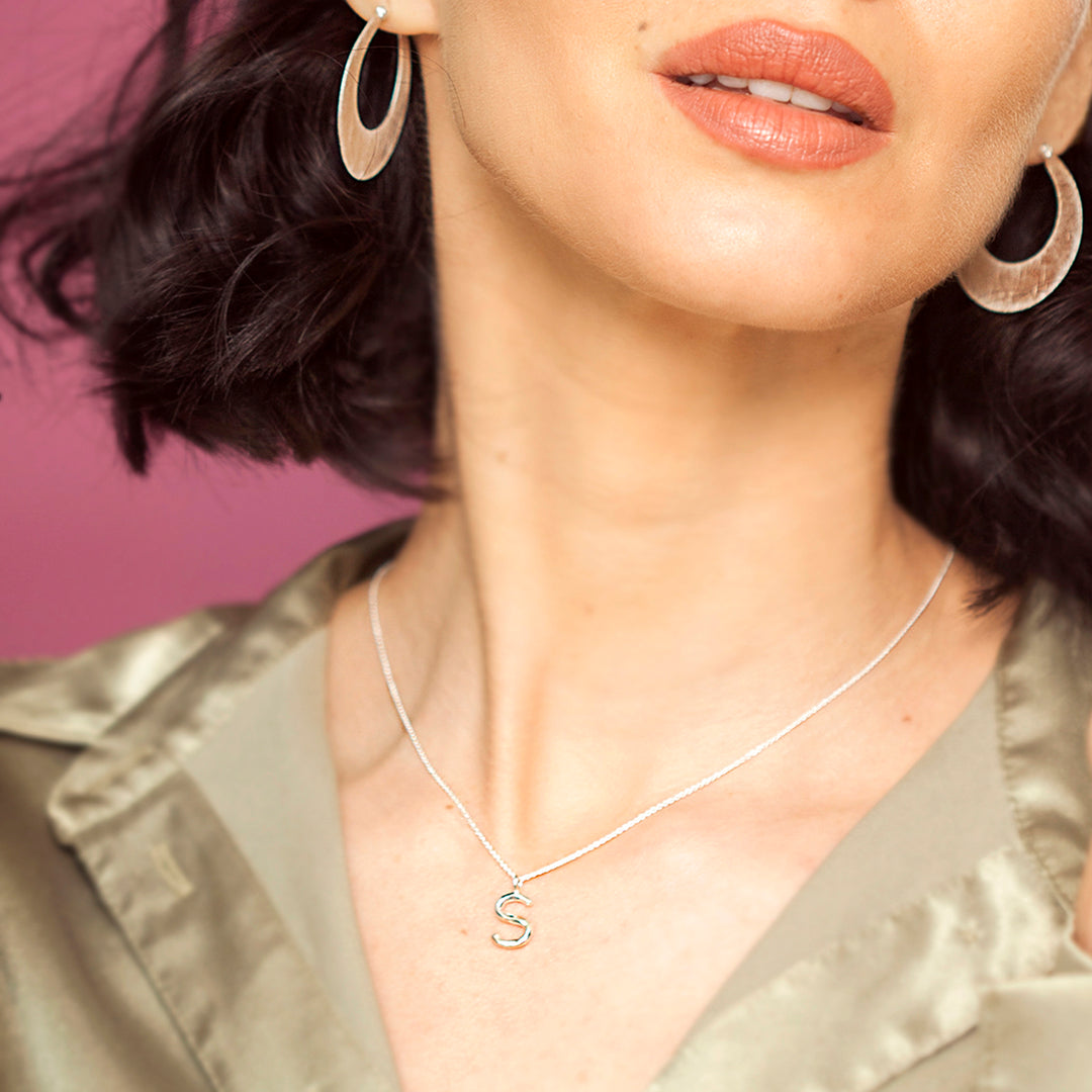 Close-up of a model wearing a silver letter S pendant and chain.