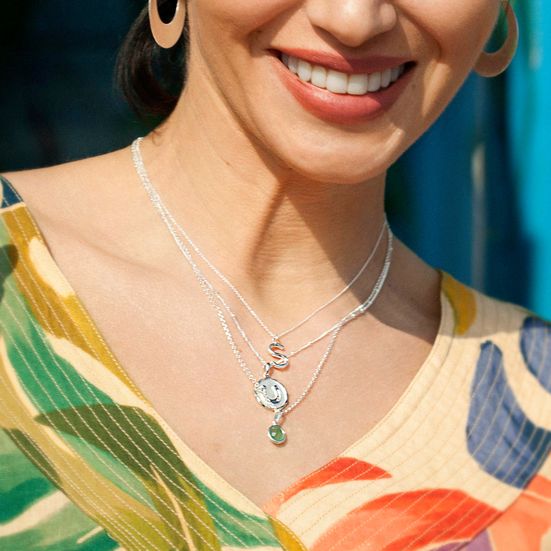 Woman wearing silver necklaces including a silver initial pendant.