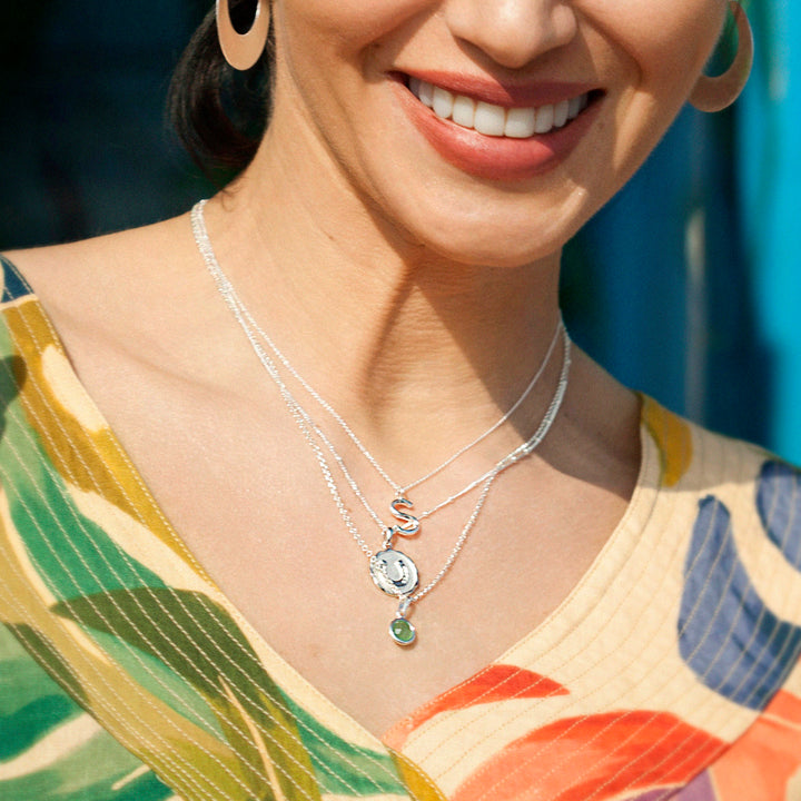 Woman wearing silver necklaces including a silver initial pendant.