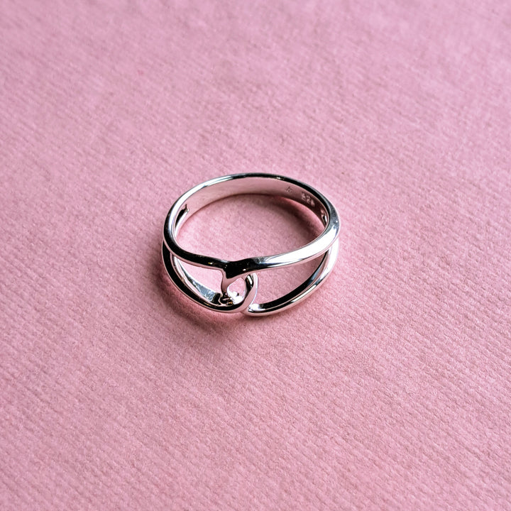 Sterling silver interlocking loop ring on a pink background
