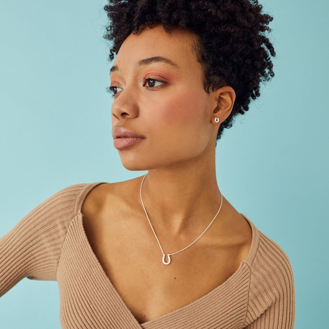 Woman wearing a sterling silver lucky horseshoe necklace and matching earrings on a light blue background