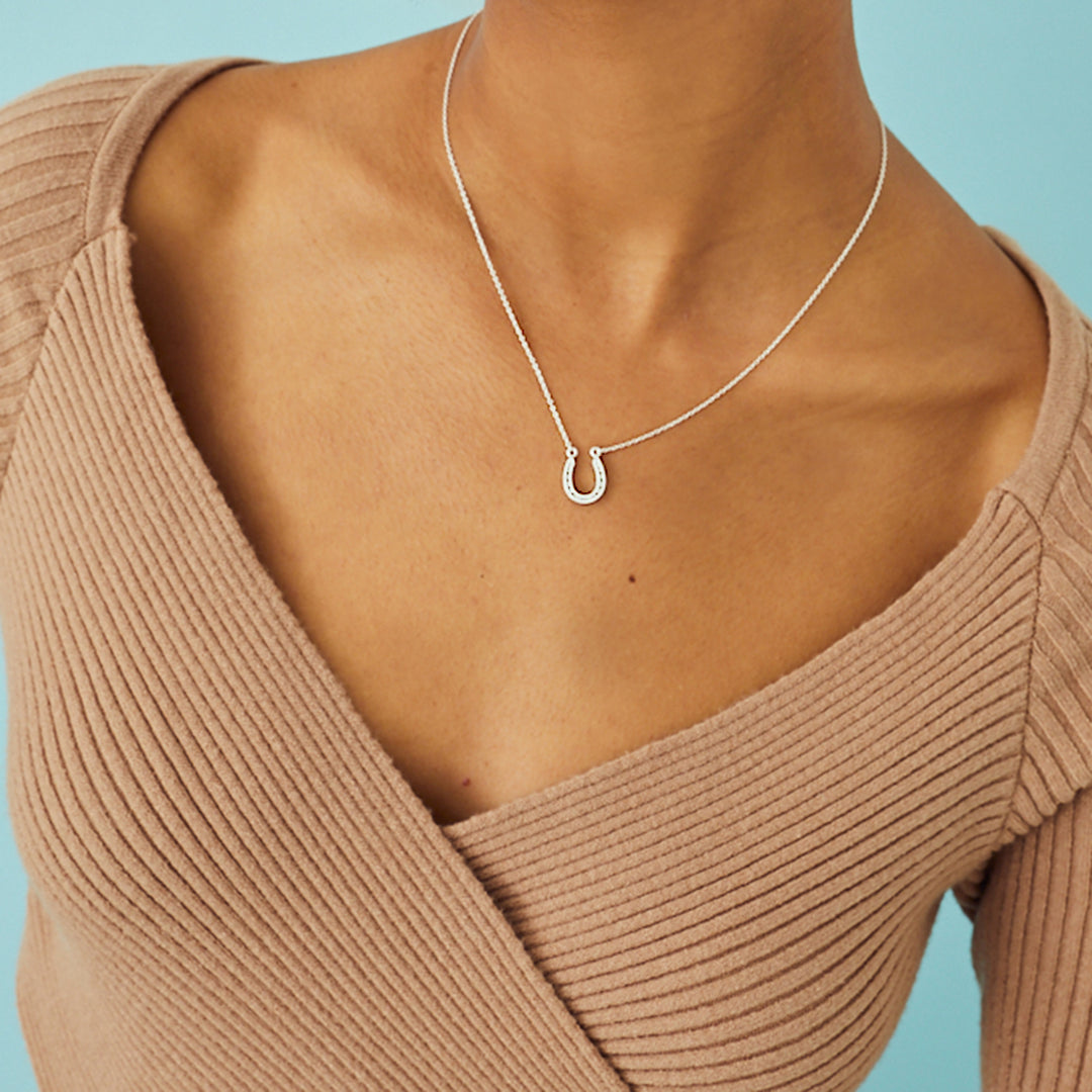 Close-up of woman wearing a sterling silver lucky horseshoe necklace on a blue background