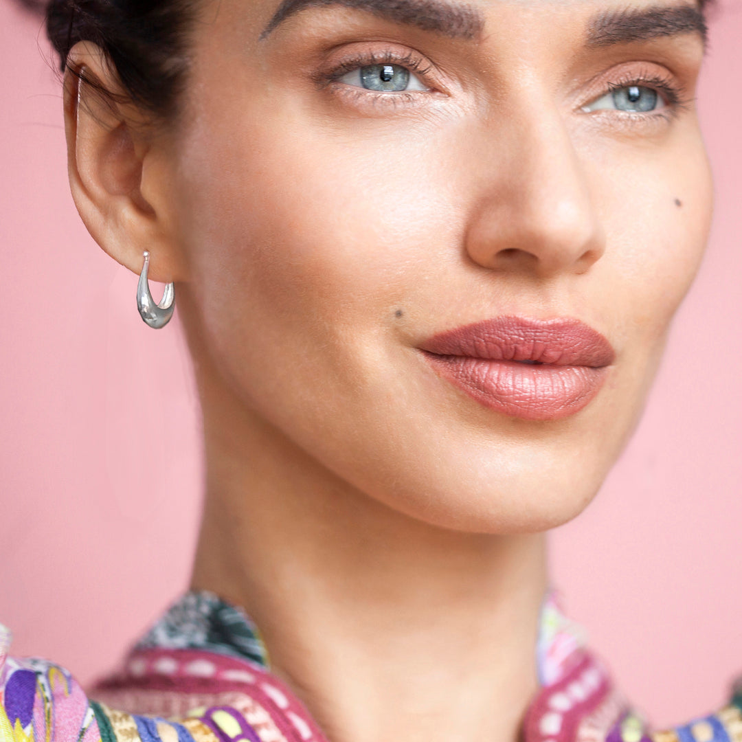 Close-up of a woman wearing a silver hoop earring against a pink background