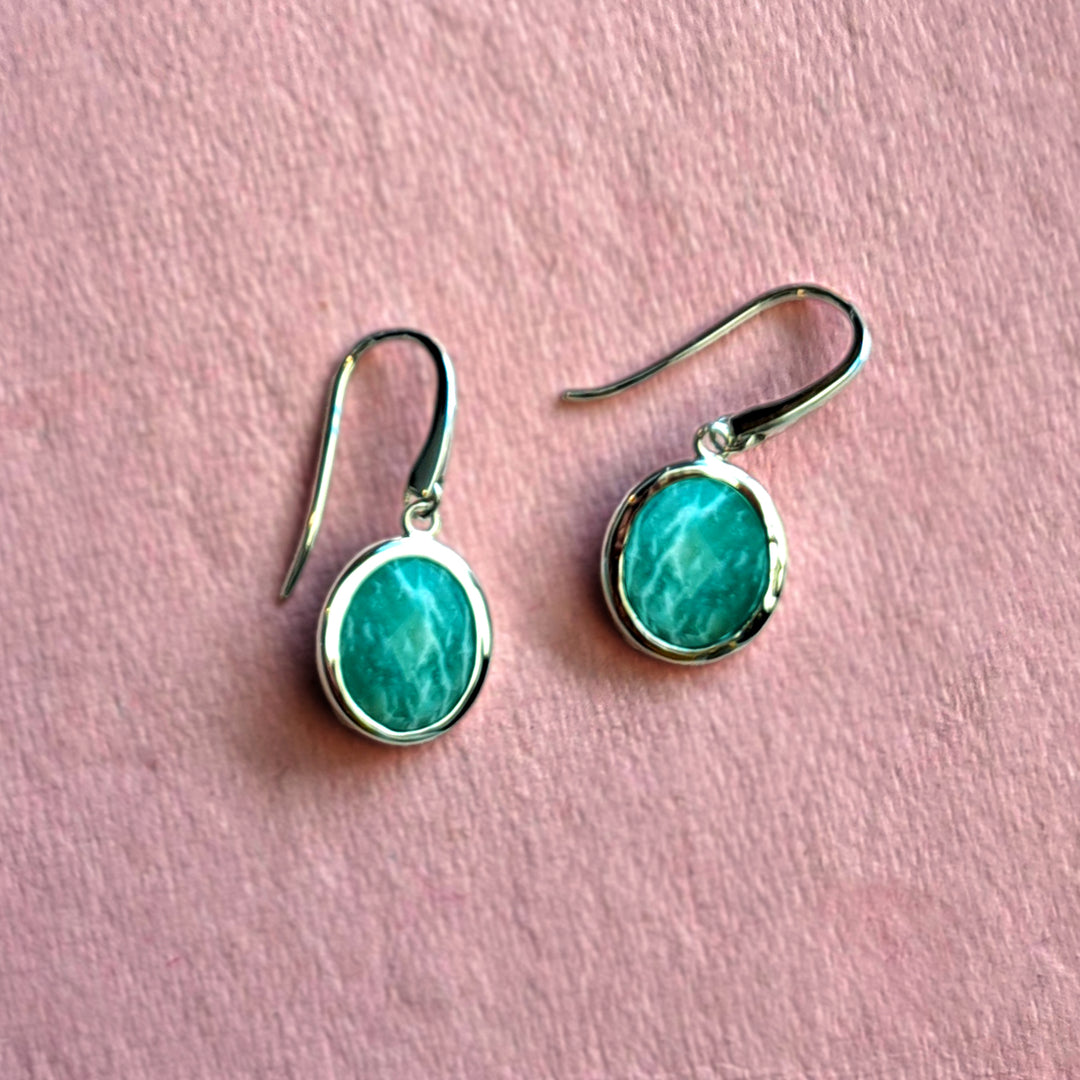 Sterling silver oval drop earrings with amazonite gemstones on a pink background