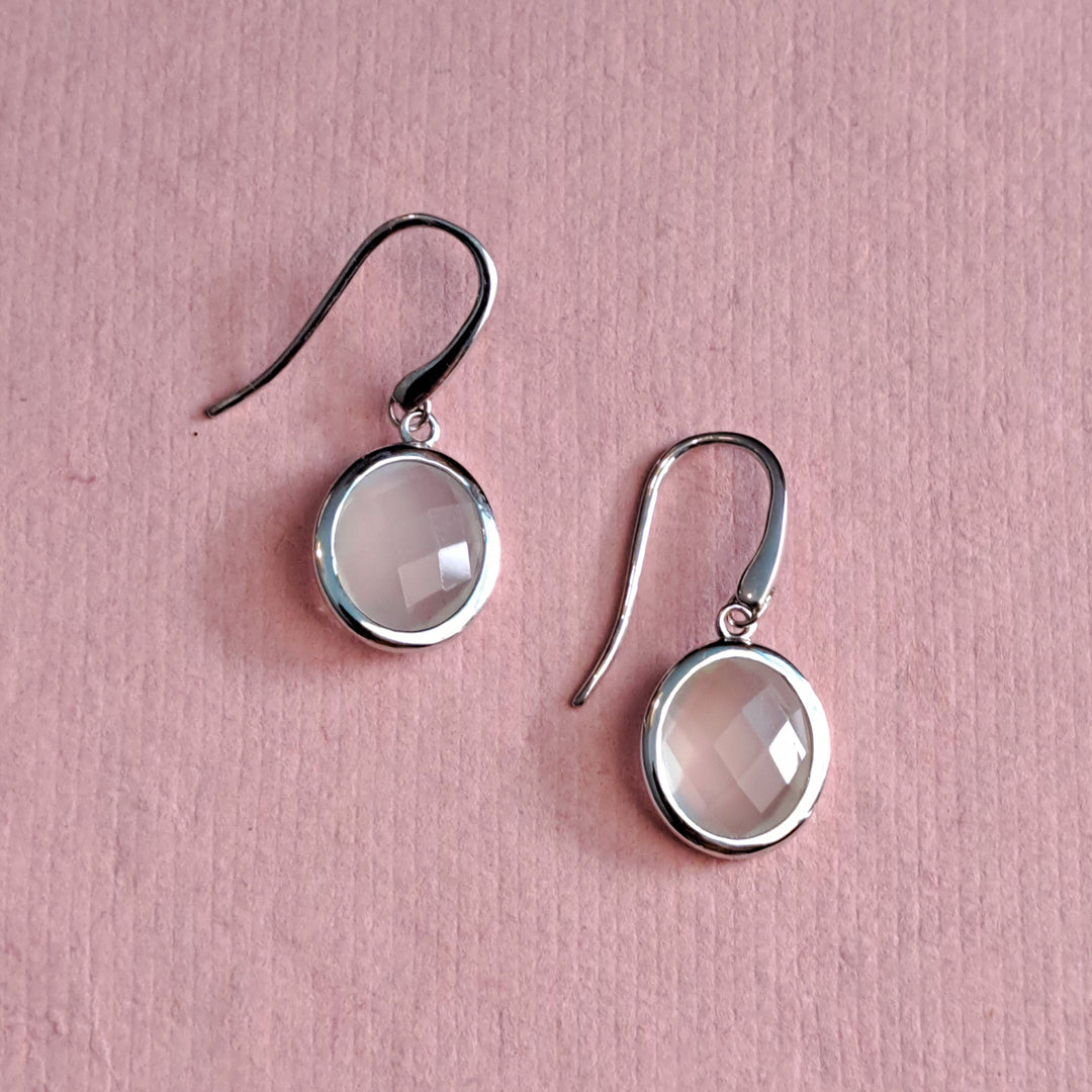 Sterling silver oval white moonstone drop earrings on an alternative pink background