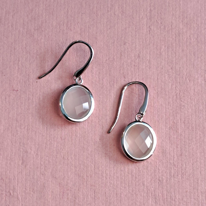 Sterling silver oval white moonstone drop earrings on an alternative pink background