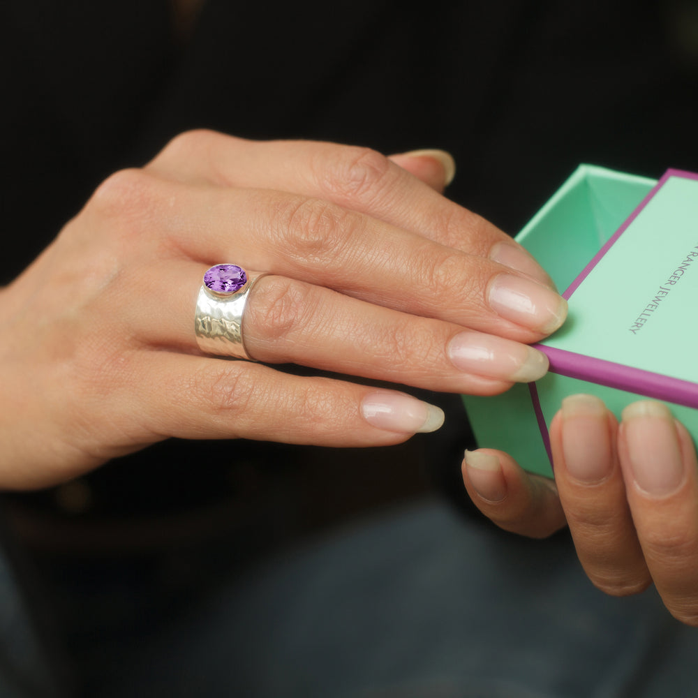 Close-up of woman wearing a sterling silver wide band ring with natural amethyst gemstone