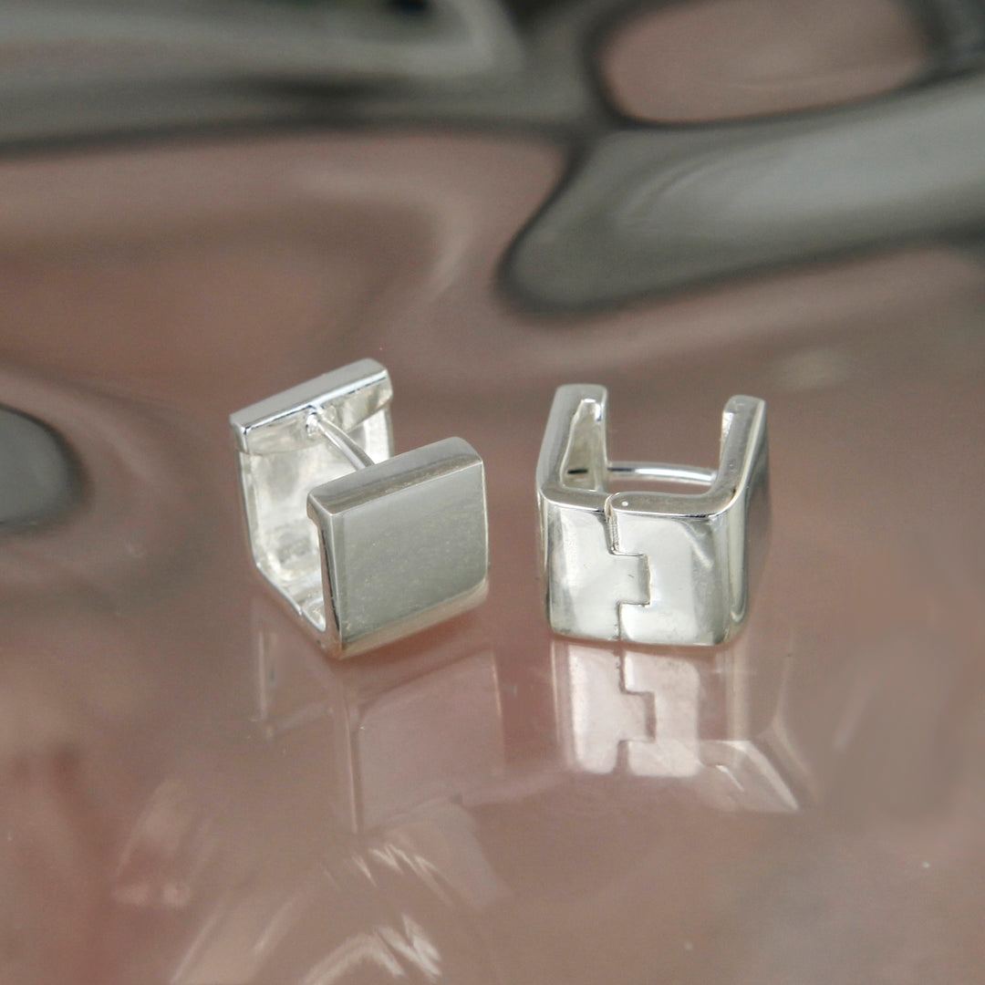 Pair of silver huggie hoop earrings on a reflective surface