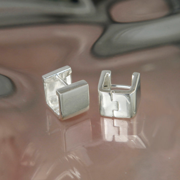 Pair of silver huggie hoop earrings on a reflective surface