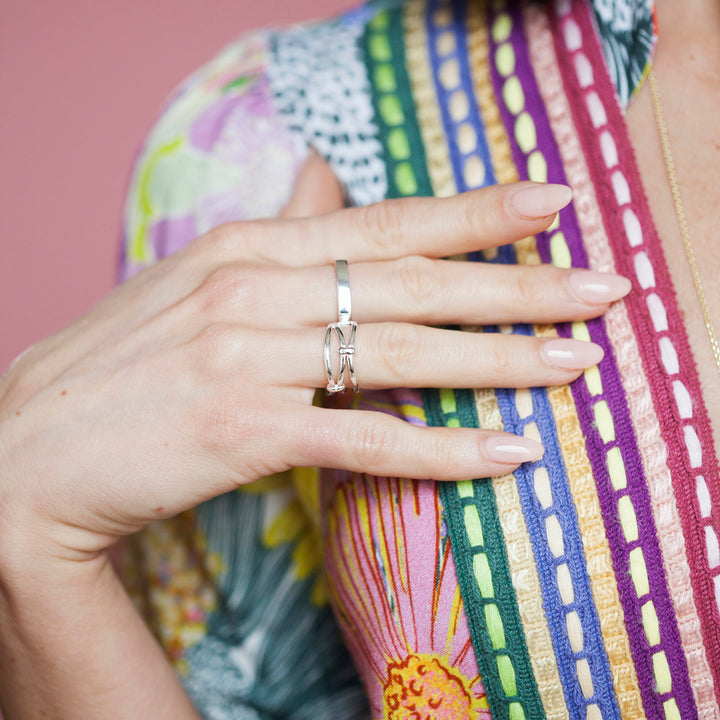 Close-up of hand with silver square and knotted rings and colourful top