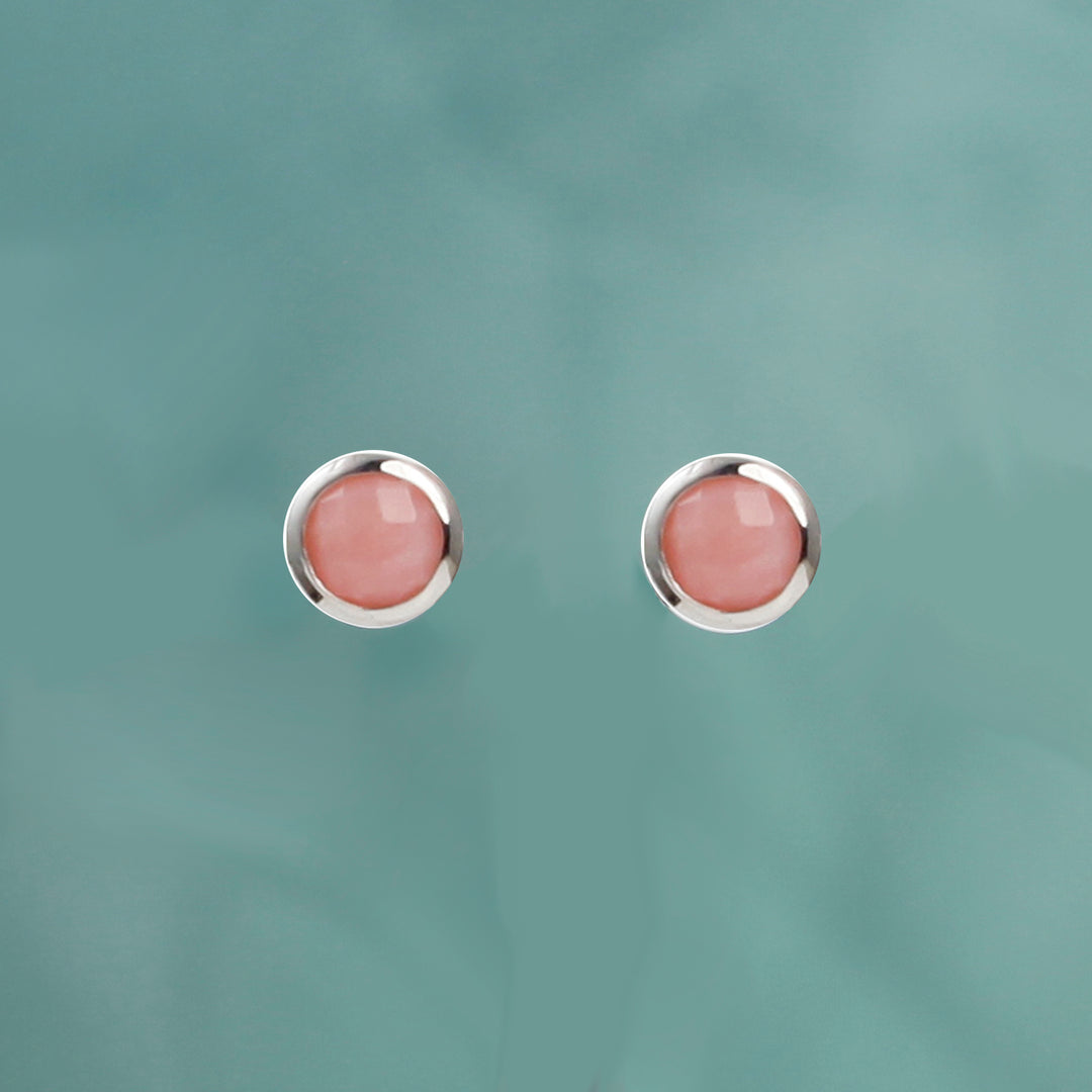 Sterling silver stud earrings set with pink opal on an aqua background