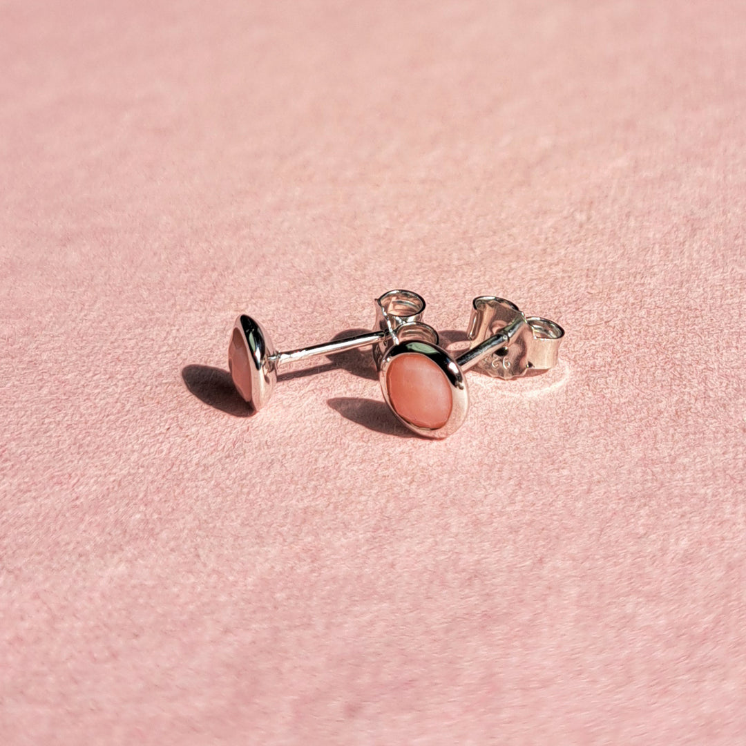 Sterling silver stud earrings set with pink opal on a pink background