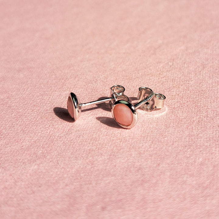 Sterling silver stud earrings set with pink opal on a pink background