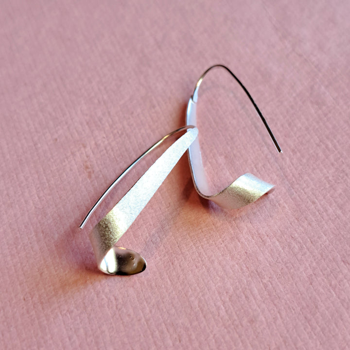 Sterling silver swirl threader hoop earrings on a pink background