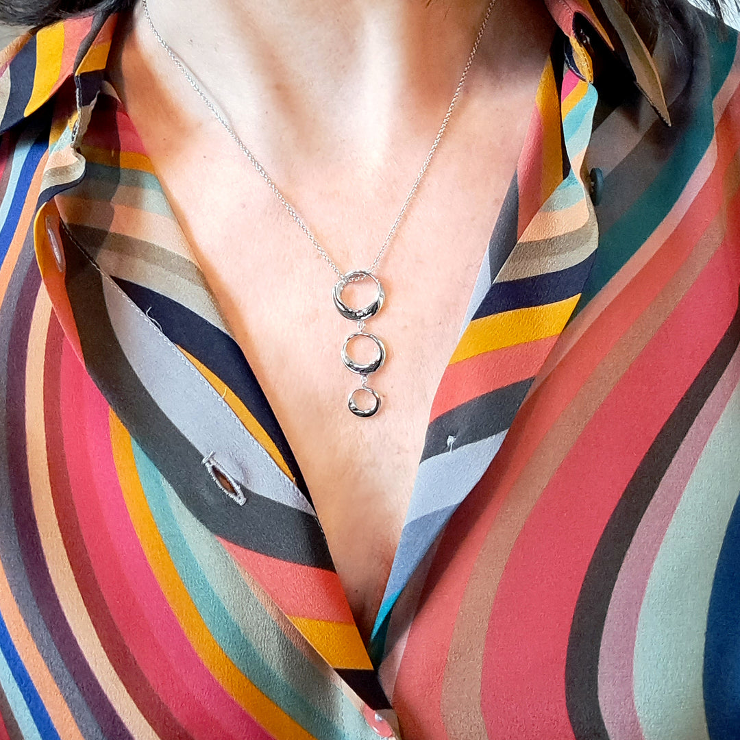 Close-up of a silver three hoop necklace with a colourful blouse