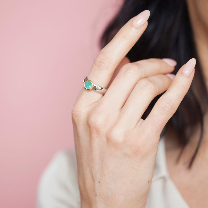 Hand wearing a silver ring with a green gemstone against a pink background