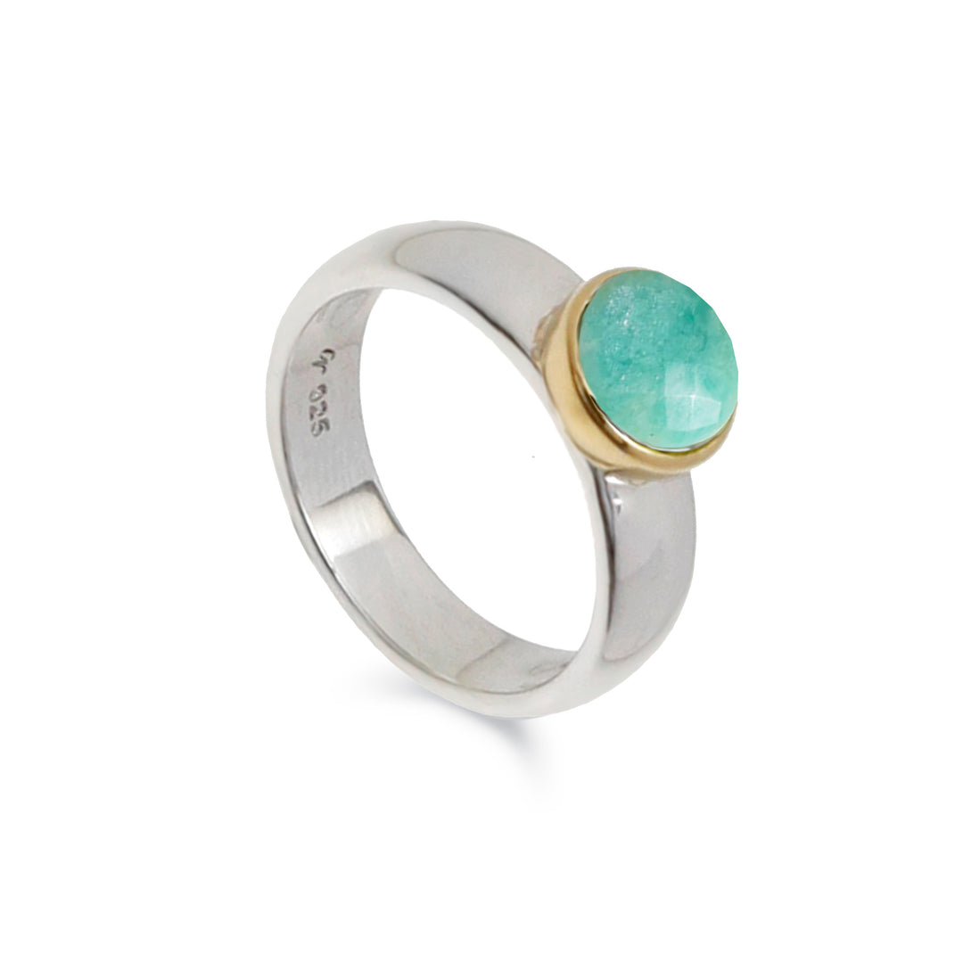 Silver ring with a round turquoise coloured stone set in gold against a white background