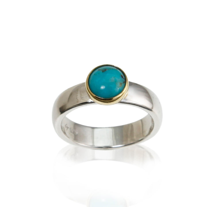 Silver and gold ring with a round turquoise stone on a white background