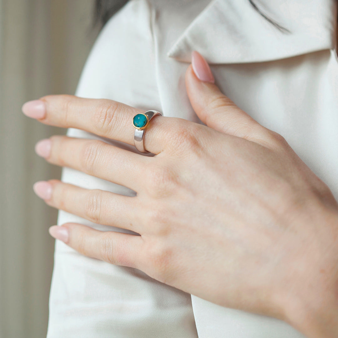 Hand wearing a silver ring with a green turquoise gemstone on a neutral background