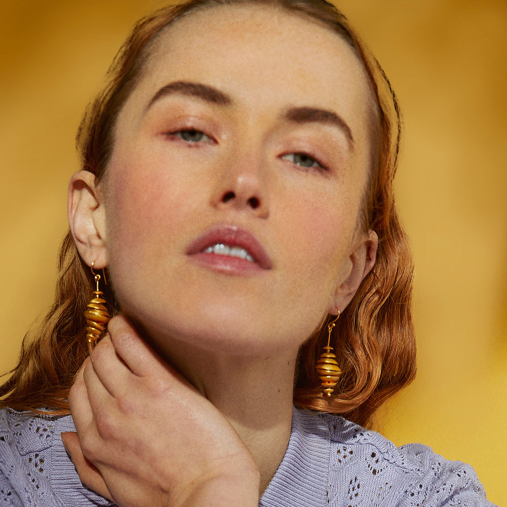 Close-up of woman wearing gold dangle earrings with a yellow background