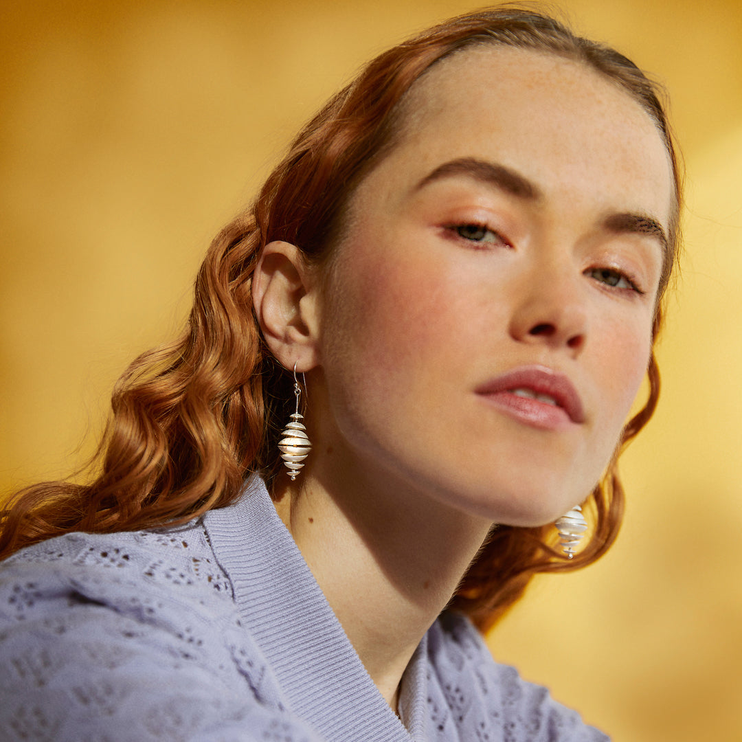 Woman with red hair wearing silver dangle earrings against a yellow background