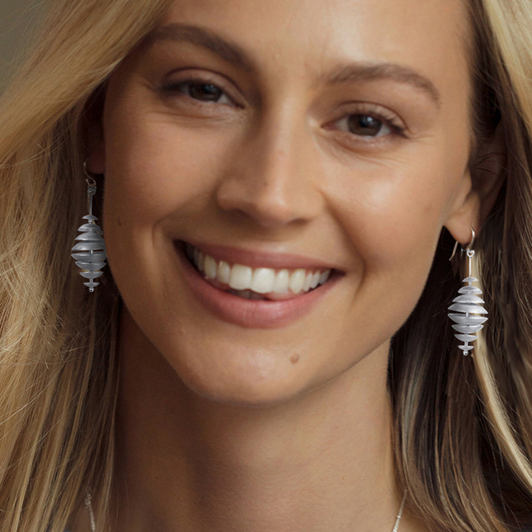 Close-up of a woman wearing silver disk earrings with a neutral background