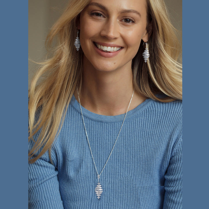 Woman wearing a blue sweater and silver necklace with matching earrings