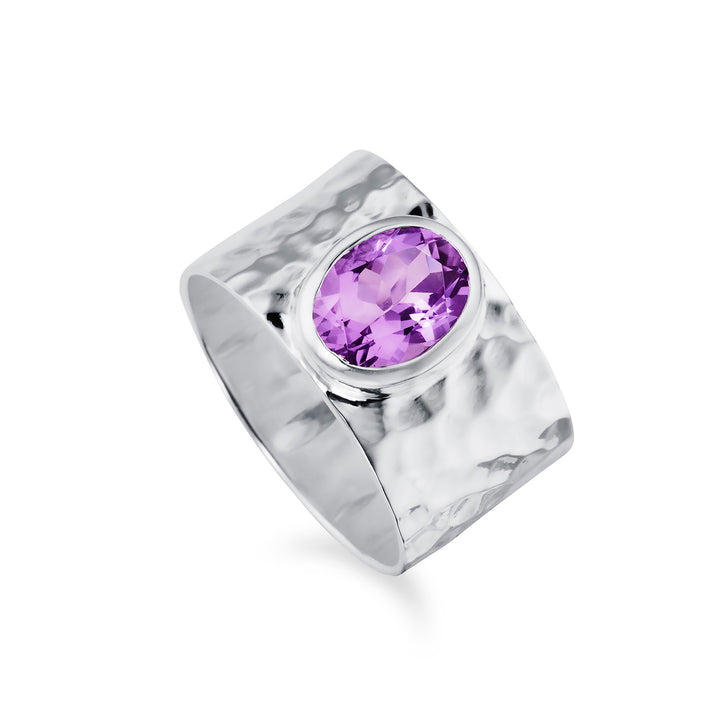 A wide silver ring with a hammered texture with a large amethyst gemstone against a white background