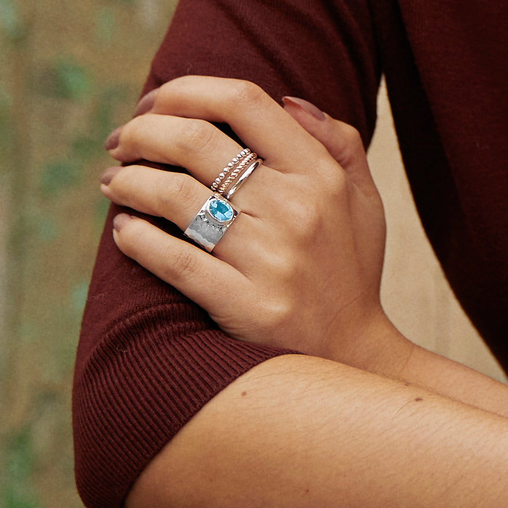 Model wearing a wide hammered silver band with a large blue topaz gemstone