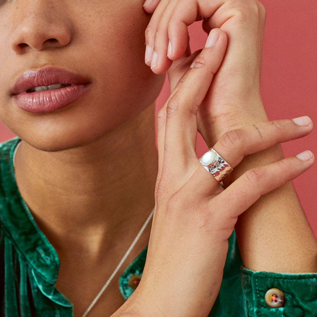 Close-up of a woman's hand wearing a wide mother-of-pearl ring with a pink background