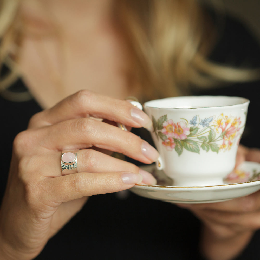 Model wearing a rose quartz statement ring holding a cup of tea