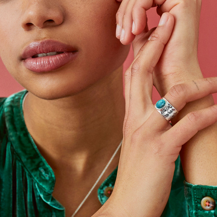 Model wearing a turquoise ring with a wide hammered band.