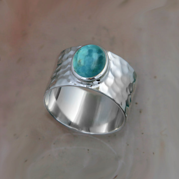 wide silver ring set with a blue stone on a reflective surface