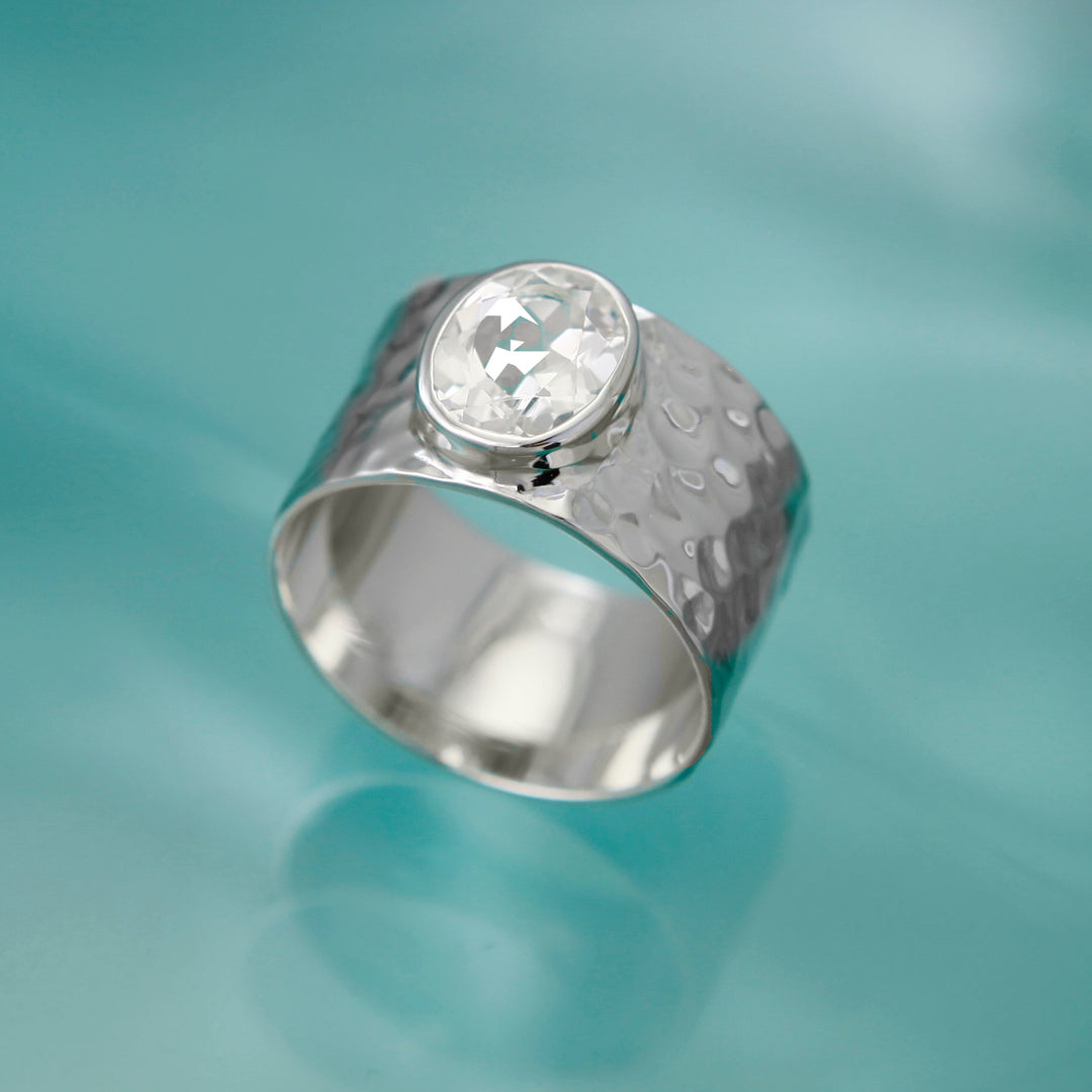 Large white topaz gemstone ring with a textured design on an aqua backgrouond