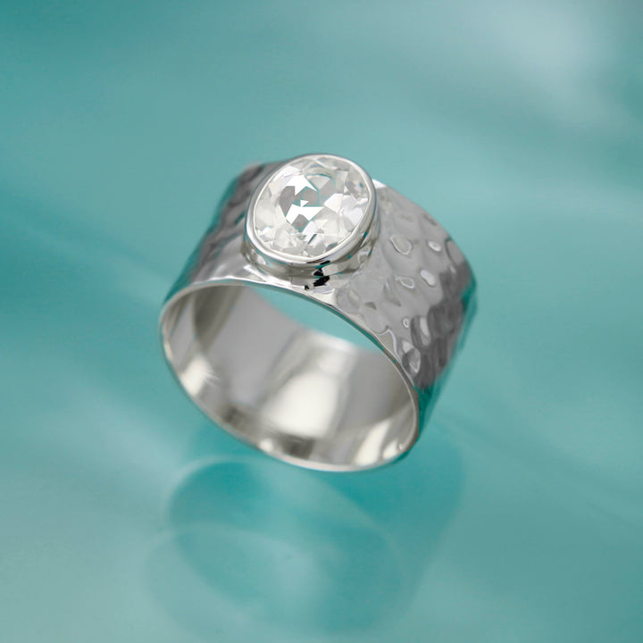 Large white topaz gemstone ring with a textured design on an aqua backgrouond