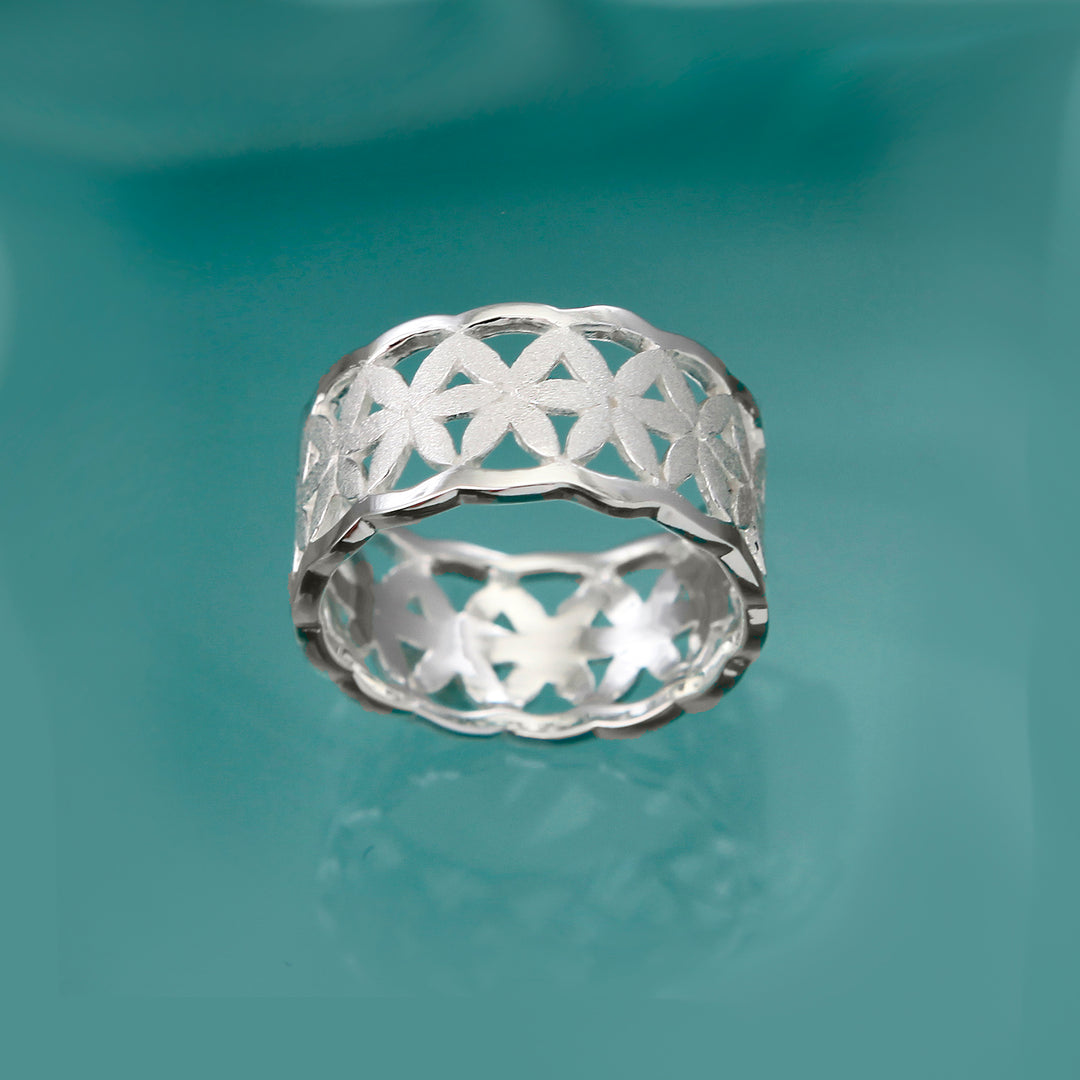 Front view of a wide matte silver ring with daisy design on an aqua background