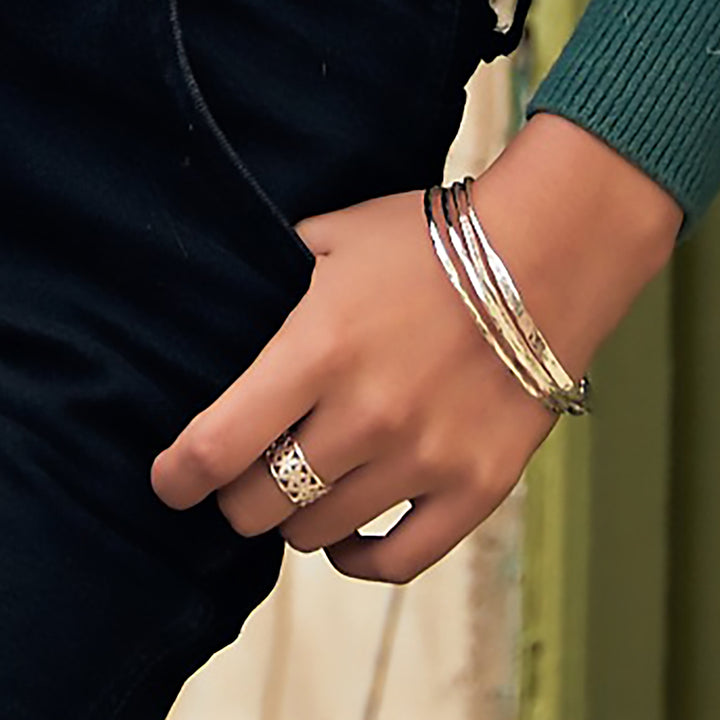 Woman wearing wide silver flower ring and multiple silver bangles