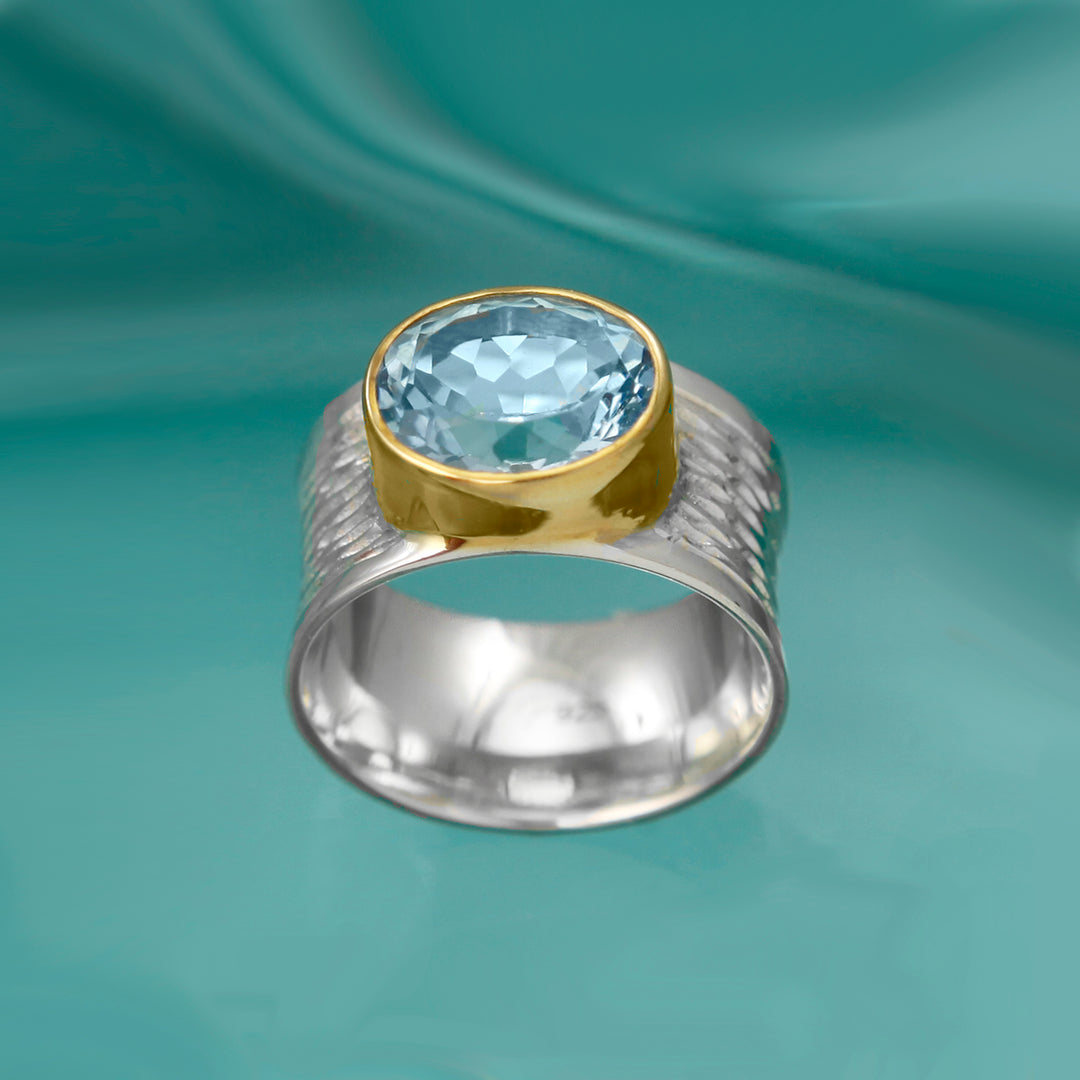 Large silver textured ring with a blue topaz gemstone with an aqua background