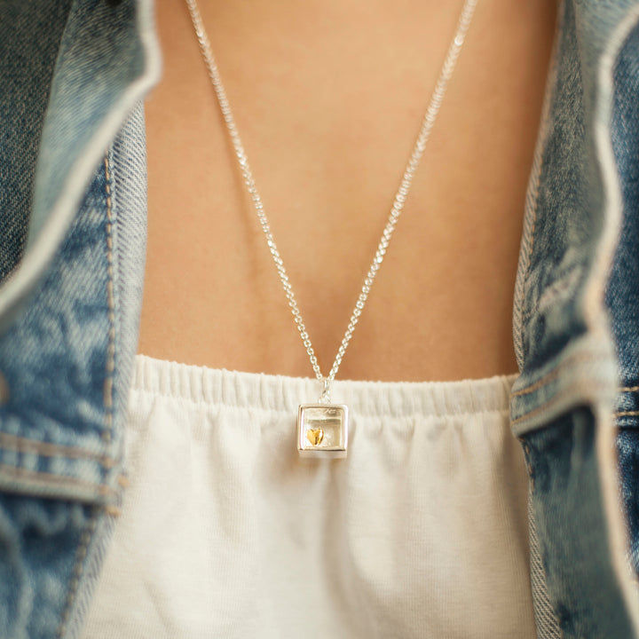 Close-up of woman wearing a sterling silver box pendant necklace with gold heart detail